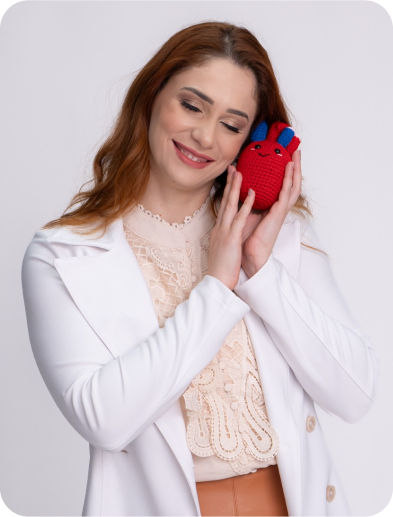 Foto da cardiologista pediatra Mariana Freitas segurando um coração de crochê ao lado do rosto.